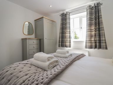 A bedroom with a bed with folded towels on it a wardrobe a chest of drawers with a mirror and a window with plaid curtains at Bettys Loft in Hawkshead