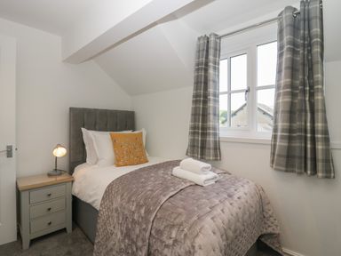 A small bedroom with a single bed bedside table lamp window and curtains at Betty's Loft in Hawkshead