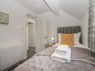 A small bedroom with a single bed white towels on the bed a grey padded headboard a bedside table with lamp and plaid curtains at Betty's Loft in Hawkshead