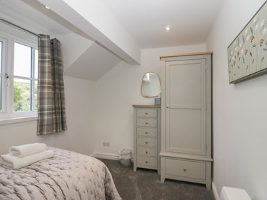 A bedroom with a bed covered in a blanket with folded towels on top and gray furniture including a chest of drawers and wardrobe at Bettys Loft in Hawkshead