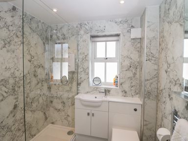 A bathroom with a shower, white vanity under a window, and marble patterned walls at Betty's Loft in Hawkshead