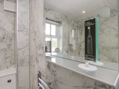 A bathroom with marble walls a window a shower a towel rail and a mirror with an electric toothbrush charging stand sign at Betty's Loft in Hawkshead