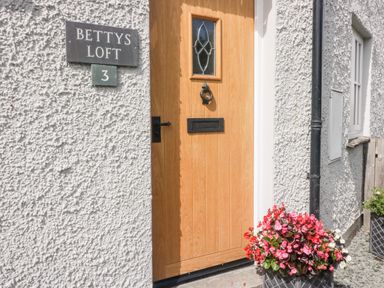 A wooden front door with a knocker and mail slot beside a sign that reads Bettys Loft 3 with a flower pot at Bettys Loft in Hawkshead