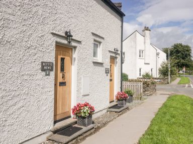 Exterior view of white buildings with wooden doors and flower pots on a sidewalk at Bettys Loft in Hawkshead