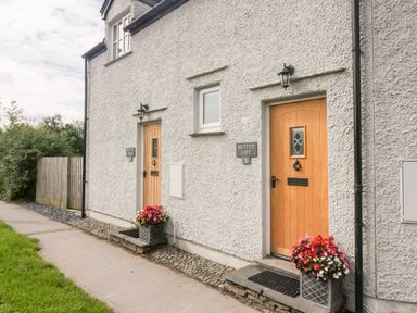 Two wooden doors with flower pots outside a white textured wall at Bettys Loft in Hawkshead