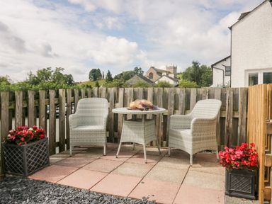 A small outdoor patio with two wicker chairs and a round table with hats on it and flowers in pots at Betty's Loft in Hawkshead