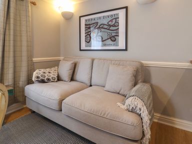 A beige sofa with cushions and throws under a framed fish artwork in a room at Braiders Rest in Bridport