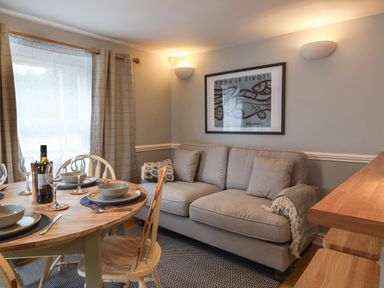 A dining area with a wooden table set with plates and glasses next to a beige sofa and framed artwork at Braiders Rest in Bridport