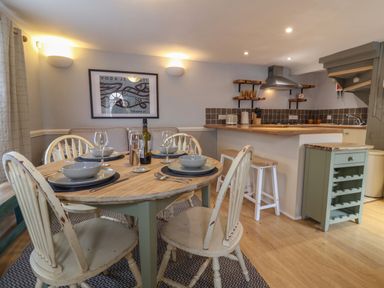A dining area with a round table set for four and an open kitchen with stools at Braiders Rest in Bridport