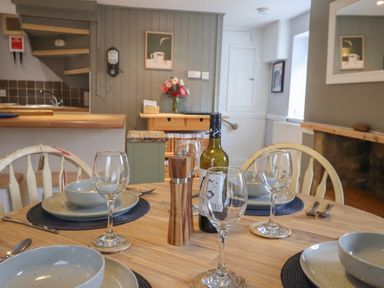 A dining table set with plates glasses a wine bottle and a pepper grinder in a kitchen area at Braiders Rest in Bridport