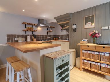A kitchen with a wooden countertop a gas stove stools wine rack and storage baskets at Braiders Rest in Bridport