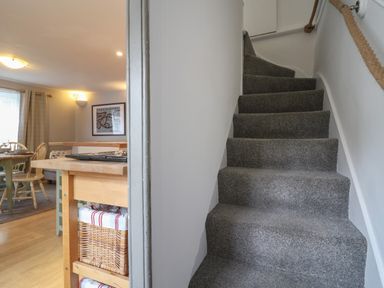 A carpeted staircase next to a kitchen area with a wooden table and chairs at Braiders Rest in Bridport