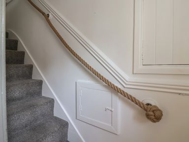 A carpeted staircase with a rope handrail and white walls at Braiders Rest in Bridport
