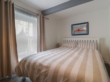 A bedroom with a double bed striped bedding a window with curtains and a framed picture on the wall at Braiders Rest in Bridport
