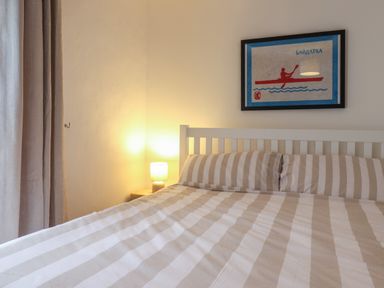 A bedroom with a bed with striped bedding a bedside lamp and framed picture on the wall at Braiders Rest in Bridport