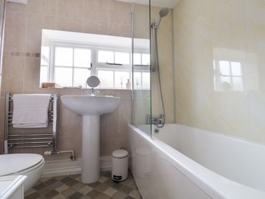 A bathroom with a bathtub shower combination a pedestal sink towel rack and a small trash bin at Braiders Rest in Bridport