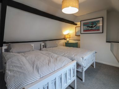 A bedroom with two single beds striped bedding a bedside table with a lamp and shark artwork on the wall at Braiders Rest in Bridport