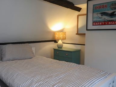 A bedroom with a single bed striped bedding bedside table lamp and framed shark poster at Braiders Rest in Bridport