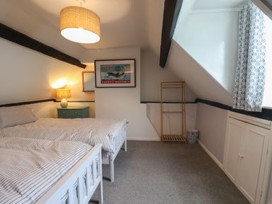 A bedroom with two single beds a side table with a lamp a framed picture a wooden rack and a window with patterned curtains at Braiders Rest in Bridport