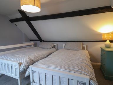 A bedroom with two single beds with striped bedding and a bedside table with lamp at Braiders Rest in Bridport