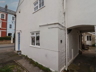A building with a blue door and white walls next to an archway and bench at Braiders Rest in Bridport