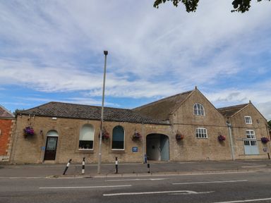 The exterior of a stone building with arched windows and doors labeled palmers brewery with hanging flower baskets in bridport