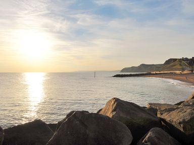 A rocky shoreline with a calm sea and a distant beach at Braiders Rest in Bridport