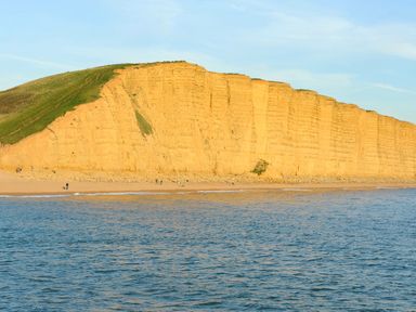 A sandy beach with people walking near yellow cliff by the sea at Braiders Rest in Bridport