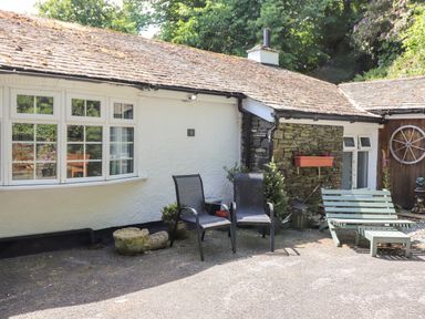 An outdoor seating area with two black chairs and a green bench in front of a white and stone building at Fell View Clappersgate near Ambleside