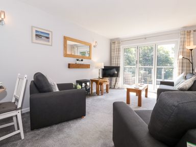 A living room with grey sofas wooden tables a wall mirror and glass doors at Fell View in Clappersgate near Ambleside