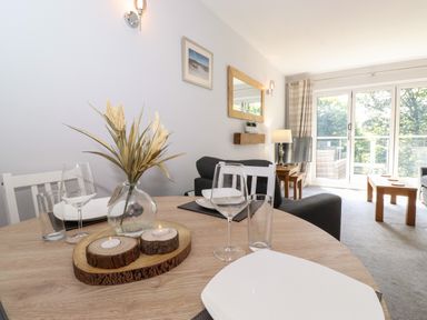 A dining table set with plates glasses and candles in a living room with sofas a lamp and large windows at Fell View in Clappersgate near Ambleside