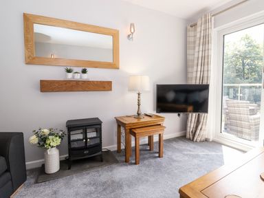 A living room with a wall mirror side table lamp tv and sliding glass door at Fell View Clappersgate near Ambleside
