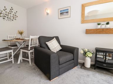 A living room with a dark armchair a round dining table with white chairs and a small fireplace at Fell View in Clappersgate near Ambleside