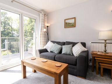 A living room with a grey sofa with cushions a wooden coffee table a side table with a lamp and glass doors leading to a balcony at Fell View Clappersgate near Ambleside