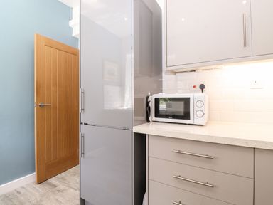 A kitchen corner with a microwave on a counter and a tall grey refrigerator next to a wooden door at Fell View Clappersgate near Ambleside
