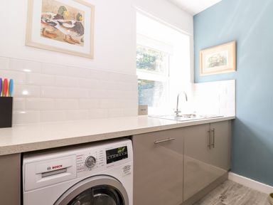 A kitchen area with a washing machine under a countertop and a sink by a window at Fell View in Clappersgate near Ambleside