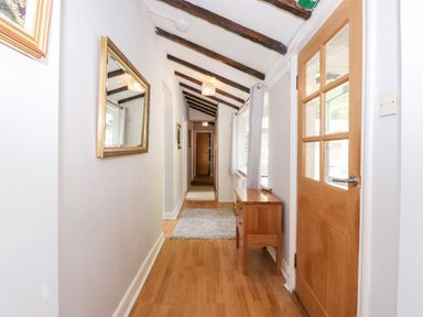 A hallway with wooden flooring wooden beams on the ceiling a wooden door a small wooden cabinet a mirror and a window with curtains at Fell View Clappersgate near Ambleside