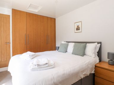 A bedroom with a bed with white linens and green pillows a wooden wardrobe a wooden bedside table with a grey lamp and a door at Fell View in Clappersgate near Ambleside