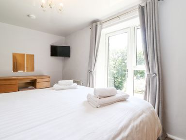 A bedroom with a bed with folded towels a wooden desk a wall-mounted TV and a window with gray curtains at Fell View in Clappersgate near Ambleside
