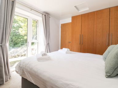 A bedroom with a bed with white linens and rolled towels near wooden wardrobes and glass doors with grey curtains at Fell View in Clappersgate near Ambleside