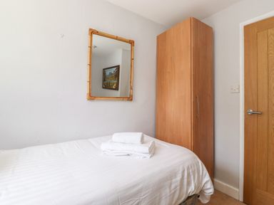 A small bedroom with a single bed white linens folded towels on the bed wooden wardrobe wooden door and wall mirror at Fell View in Clappersgate near Ambleside