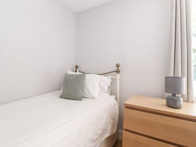 A bedroom with a single bed with white bedding a green pillow and a wooden dresser with a grey lamp at Fell View Clappersgate near Ambleside