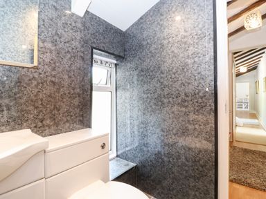 A small bathroom with a toilet and sink next to a window and a hallway with exposed wooden beams at Fell View in Clappersgate near Ambleside