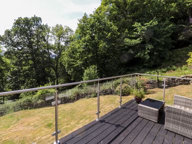 A patio with rattan chairs and a table overlooking a garden with trees at Fell View in Clappersgate near Ambleside