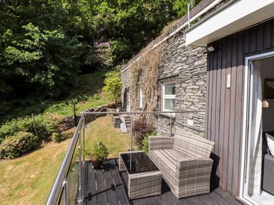 An outdoor patio with a wicker loveseat and table overlooking a garden and stone wall at Fell View in Clappersgate near Ambleside