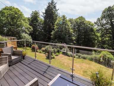 A balcony with outdoor chairs a glass railing and a lawn with trees at Fell View in Clappersgate near Ambleside