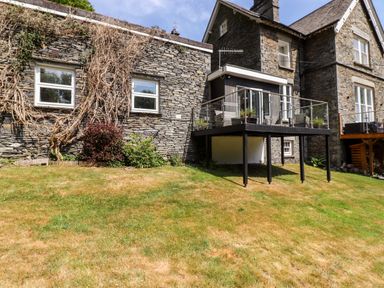 A stone building with a raised glass balcony and grassy yard at Fell View in Clappersgate near Ambleside