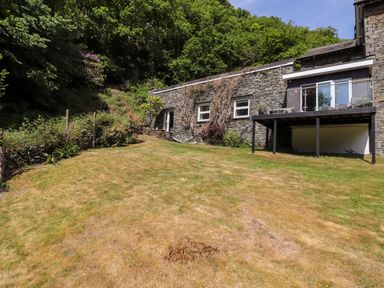 A backyard with lawn shrubbery and stone house with balcony at Fell View in Clappersgate near Ambleside