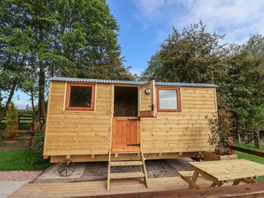 A wooden hut on wheels with two windows and an open door next to a picnic table outside at The Oak Hut in Coton near Whitchurch
