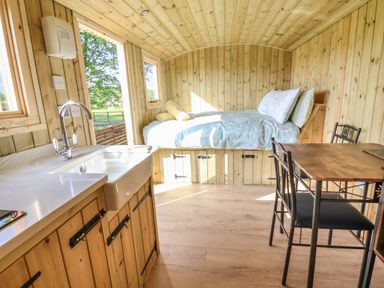 A small wooden room with a kitchen sink dining table chairs and a bed at The Oak Hut in Coton near Whitchurch